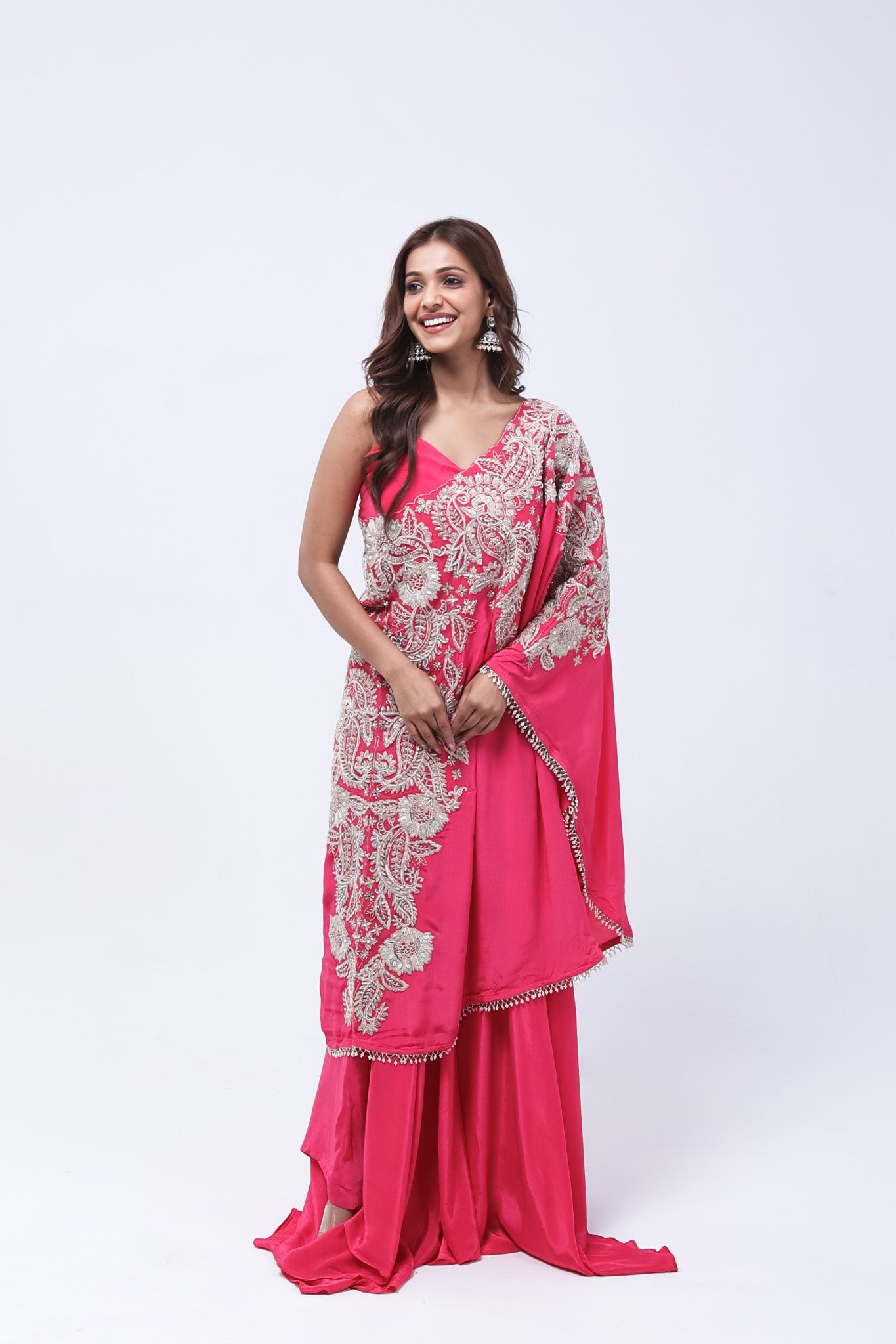 Woman wearing a pink traditional  one shoulder outfit with white embroidery on a white background