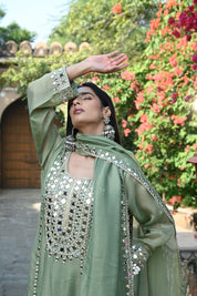 Sage-green traditional outfit featuring a mirror-embroidered kurta with wide sleeves, matching wide-legged trousers with embellished hems, and a coordinating dupatta finished with reflective detailing and tassels.