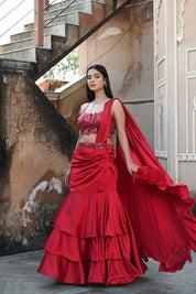 Model wearing a deep red embellished lehenga set with a sequined blouse, layered flared skirt, and flowing cape-style dupatta, styled with statement jewellery, posed in a heritage courtyard for Tulsi Studio Lifestyle wedding collection.