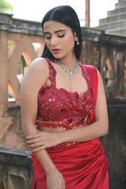 Model wearing a deep red embellished lehenga set with a sequined blouse, layered flared skirt, and flowing cape-style dupatta, styled with statement jewellery, posed in a heritage courtyard for Tulsi Studio Lifestyle wedding collection.