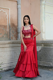 Model wearing a deep red embellished lehenga set with a sequined blouse, layered flared skirt, and flowing cape-style dupatta, styled with statement jewellery, posed in a heritage courtyard for Tulsi Studio Lifestyle wedding collection.