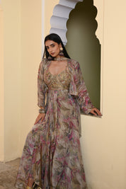 Model wearing a pastel floral printed Anarkali gown with an embroidered bustier and sheer jacket, styled with statement earrings and bangles, posing against a heritage archway for Tulsi Studio festive collection.