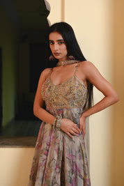 Model wearing a pastel floral printed Anarkali gown with an embroidered bustier and sheer jacket, styled with statement earrings and bangles, posing against a heritage archway for Tulsi Studio festive collection.