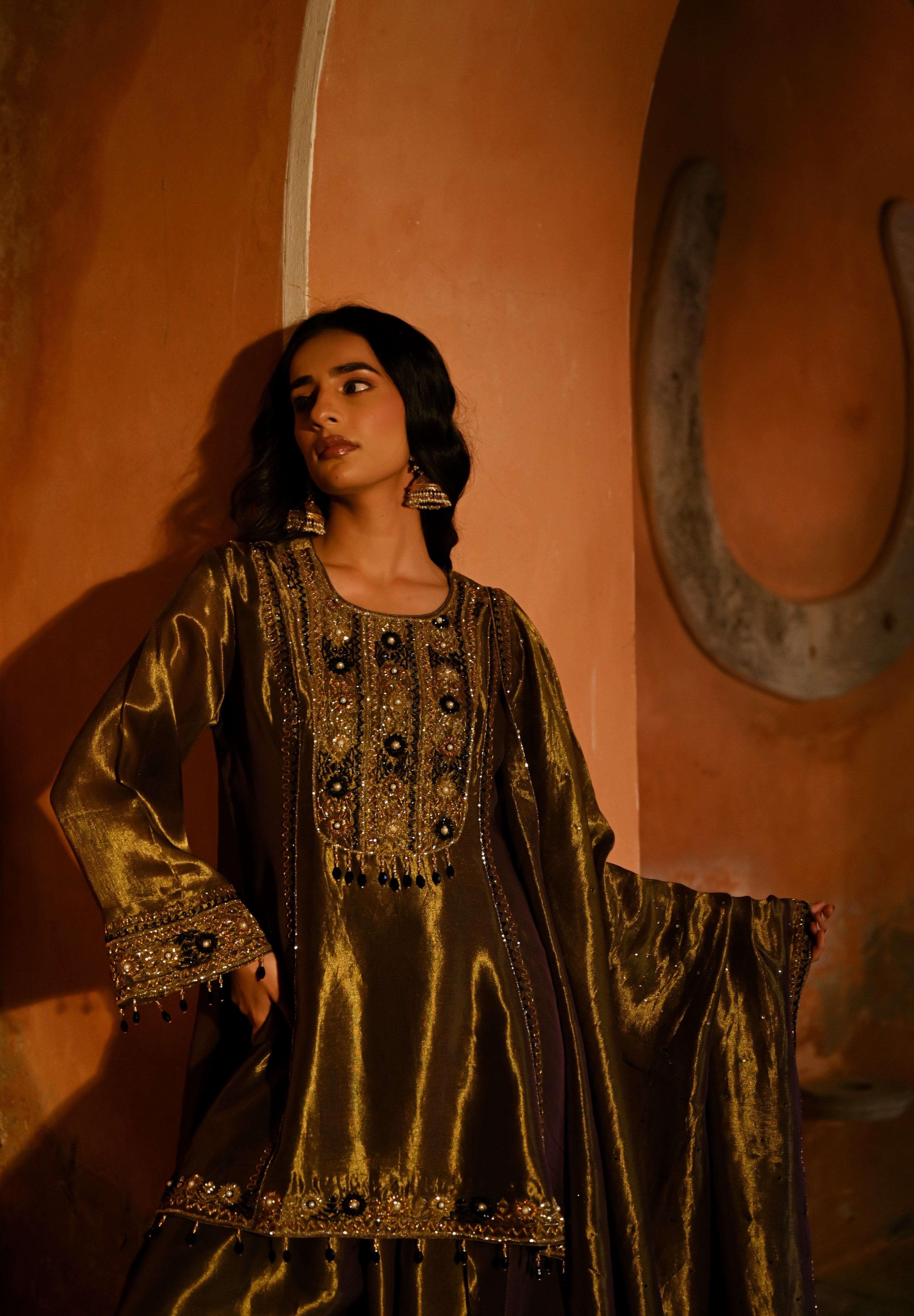 Woman in a traditional outfit standing against an orange wall with a horseshoe decoration.