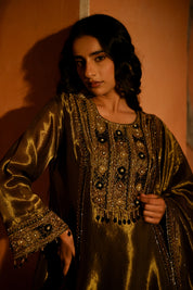 Woman in a gold embroidered traditional outfit against an orange wall.