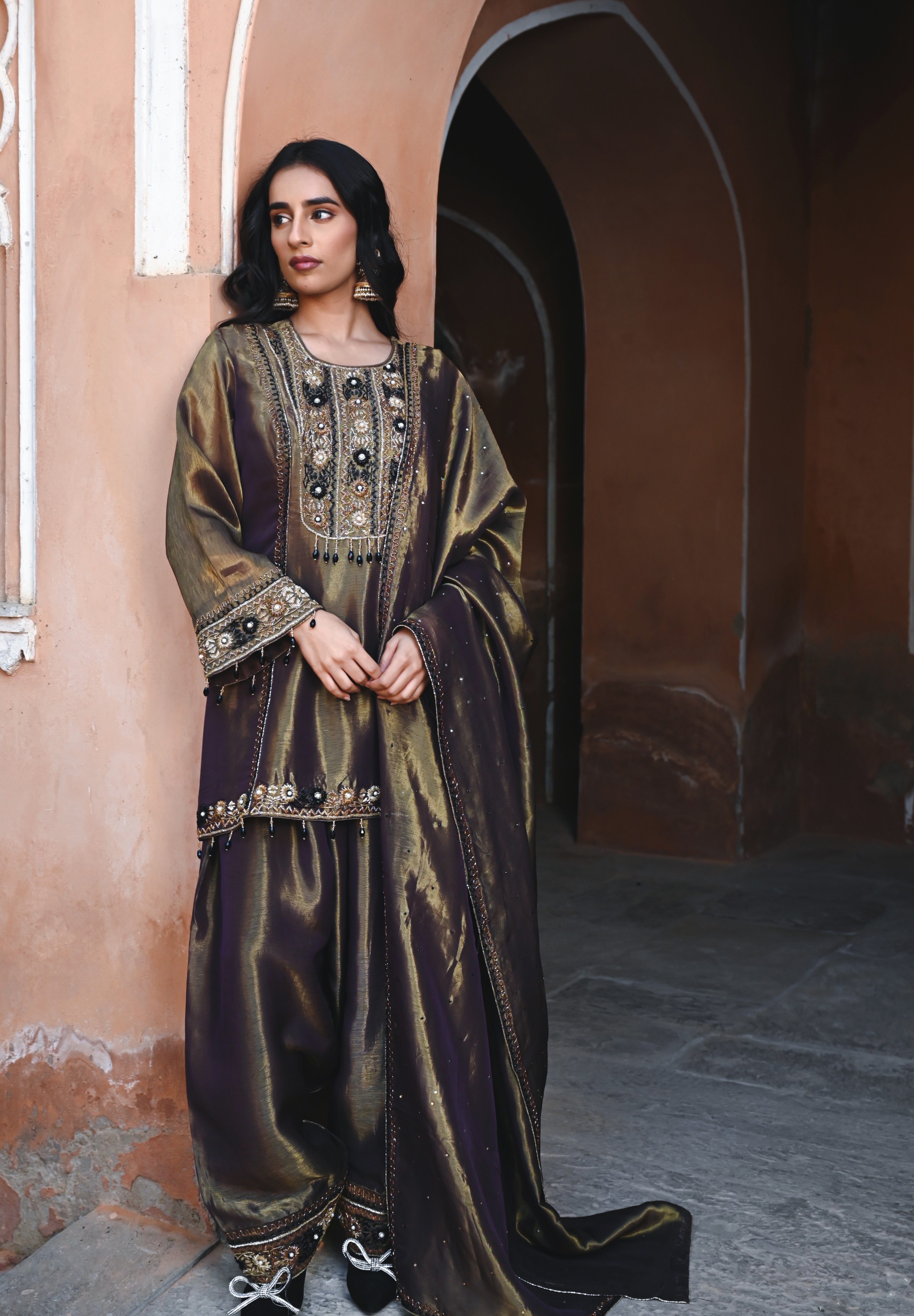 Woman in an ornate traditional outfit standing in a historic architectural setting.