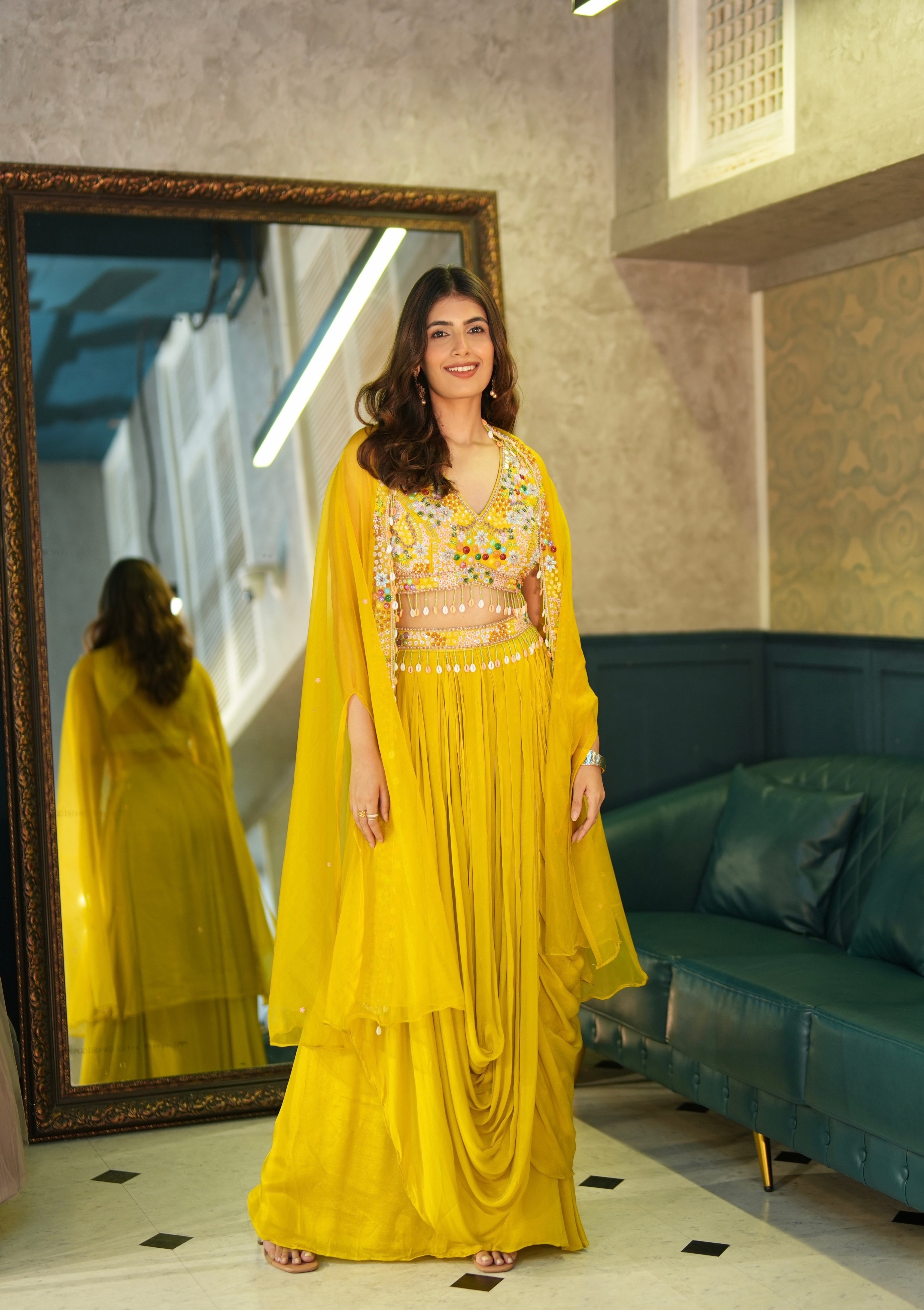 Woman in a yellow traditional outfit standing in front of a mirror in a room with a green sofa.