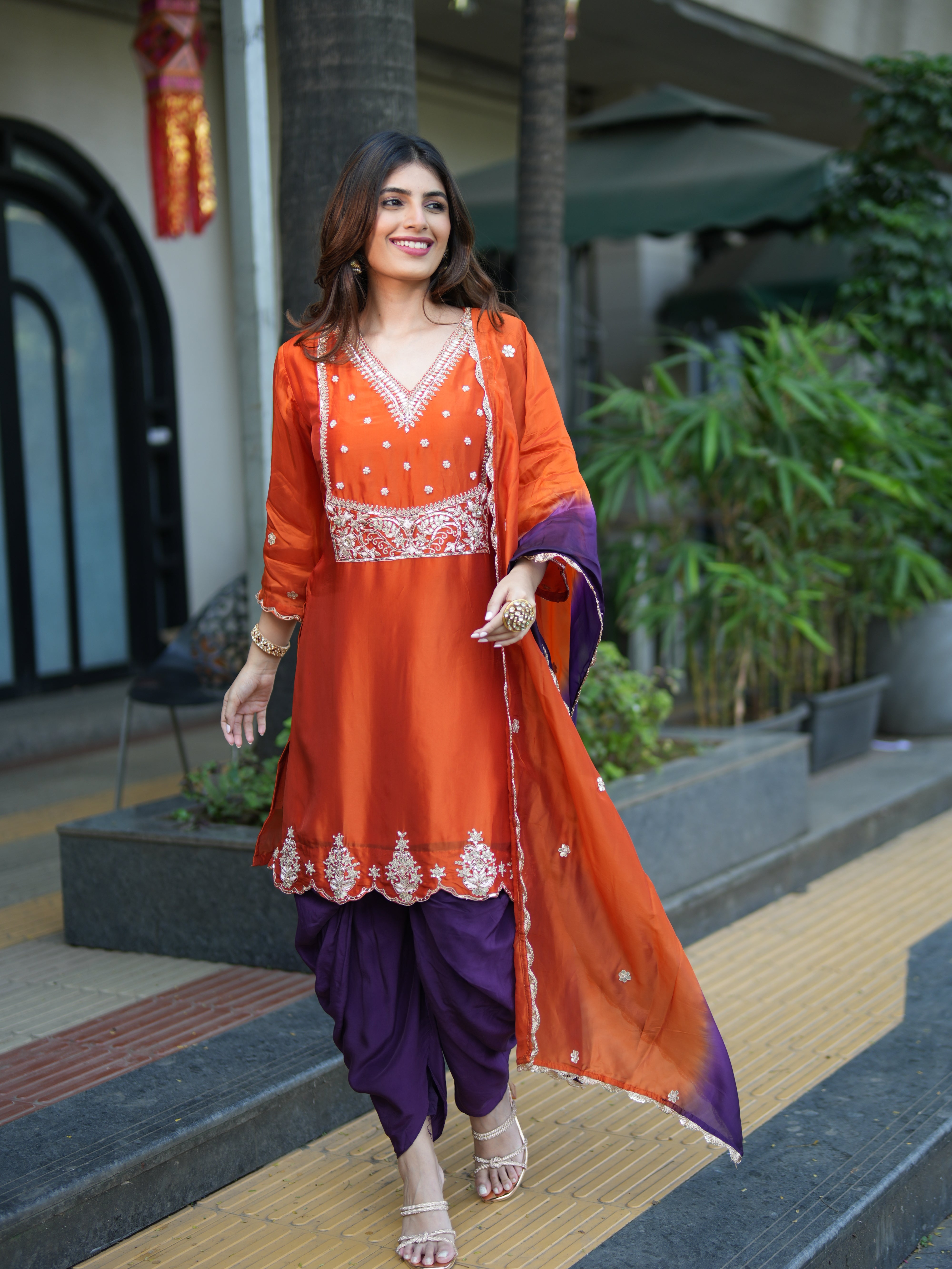 Woman in an orange and purple traditional outfit standing outdoors.