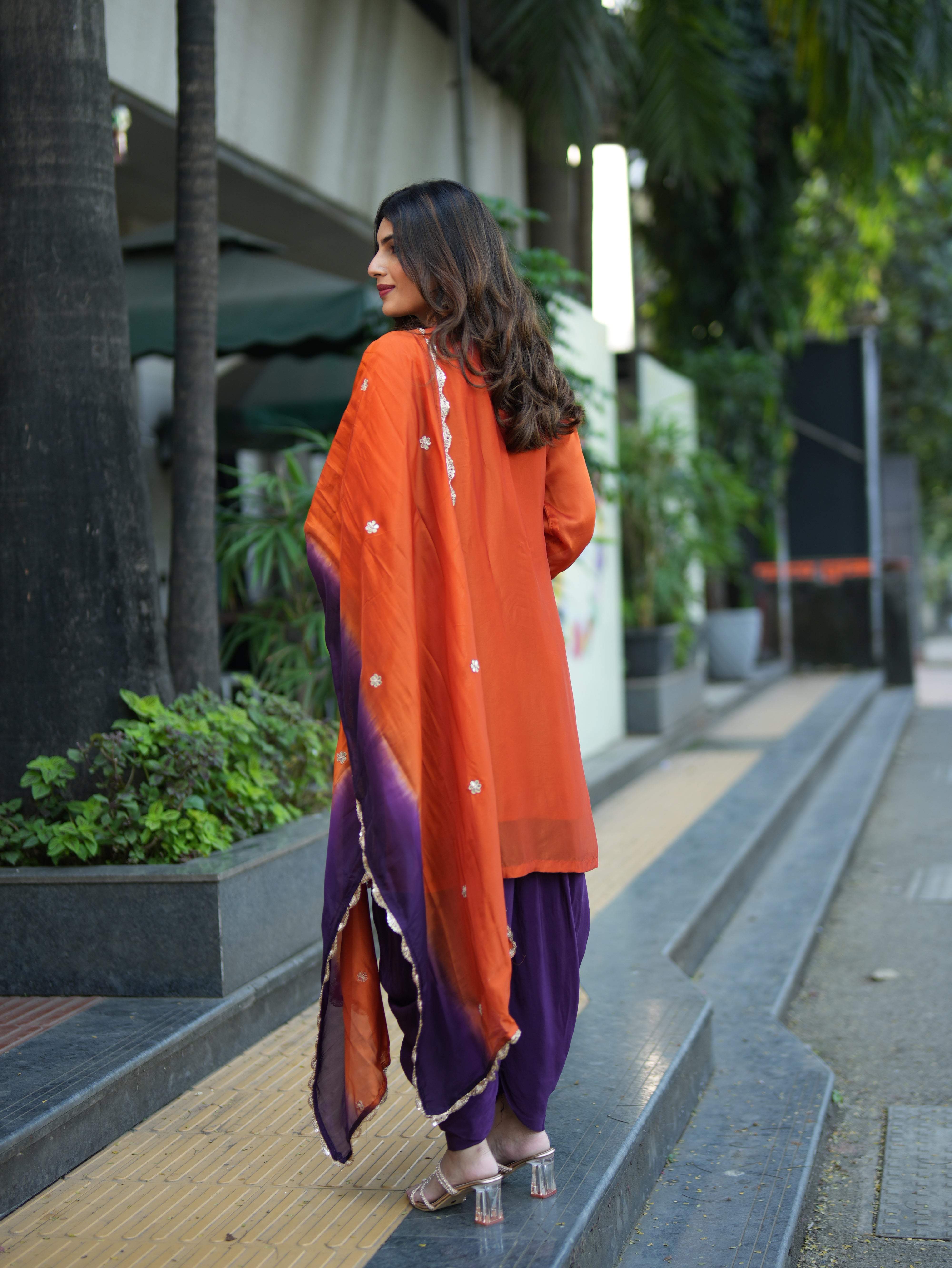 Woman in an orange and purple traditional outfit walking outdoors.