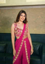 Woman in a pink indo western saree with gold embroidery standing against a patterned wall.