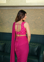 Woman in a pink indo western saree with a patterned wall and green sofa in the background