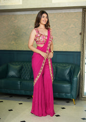 Woman in a pink indo western saree with a green sofa and patterned wall in the background