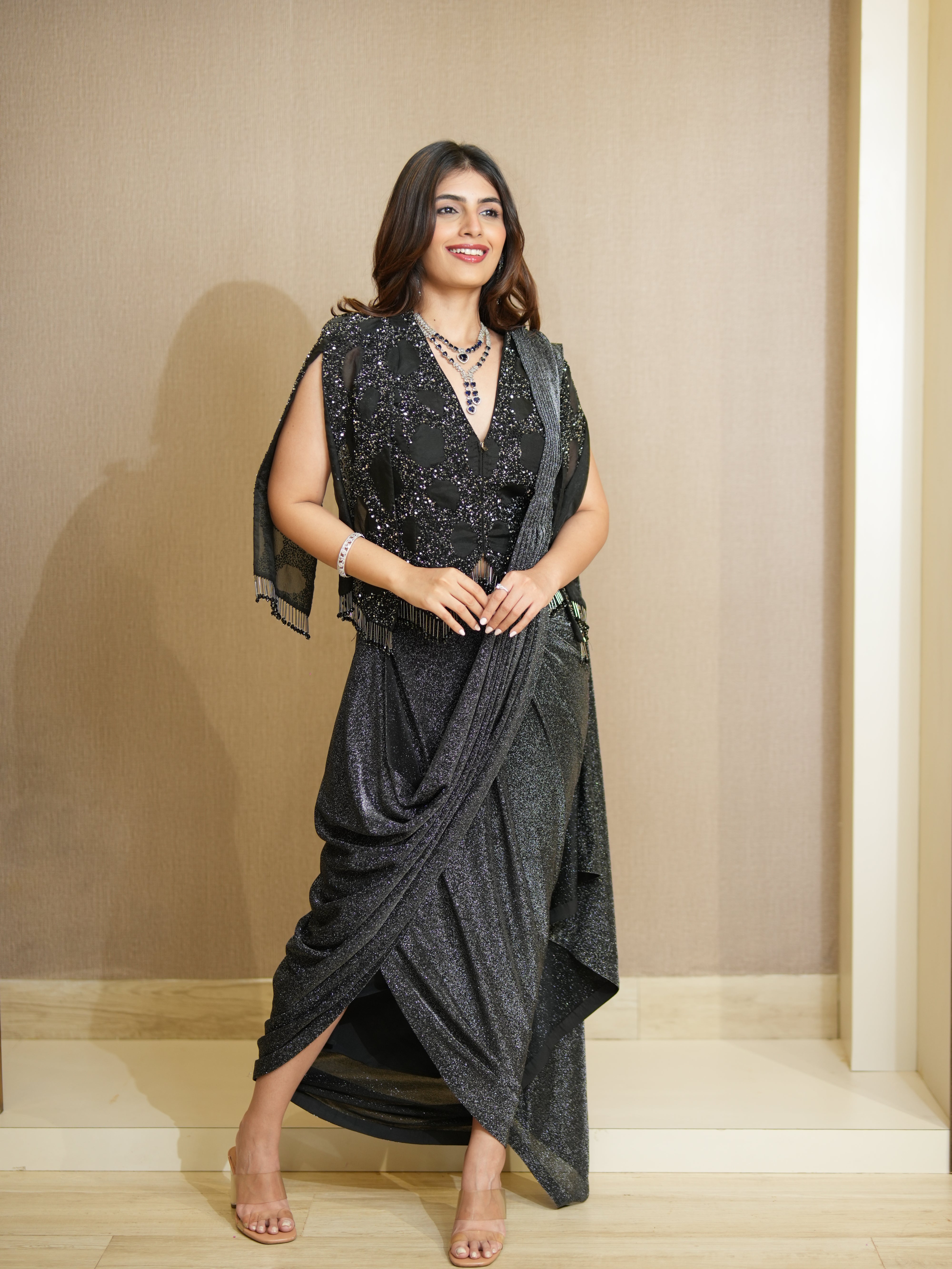 Woman in a black sequined dress standing against a beige wall.