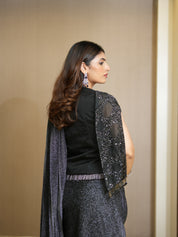 Woman wearing a black top and gray skirt with a matching shawl against a beige background