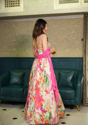 Woman in a colorful floral dress with a pink sash standing in a room with green leather couches and patterned walls.