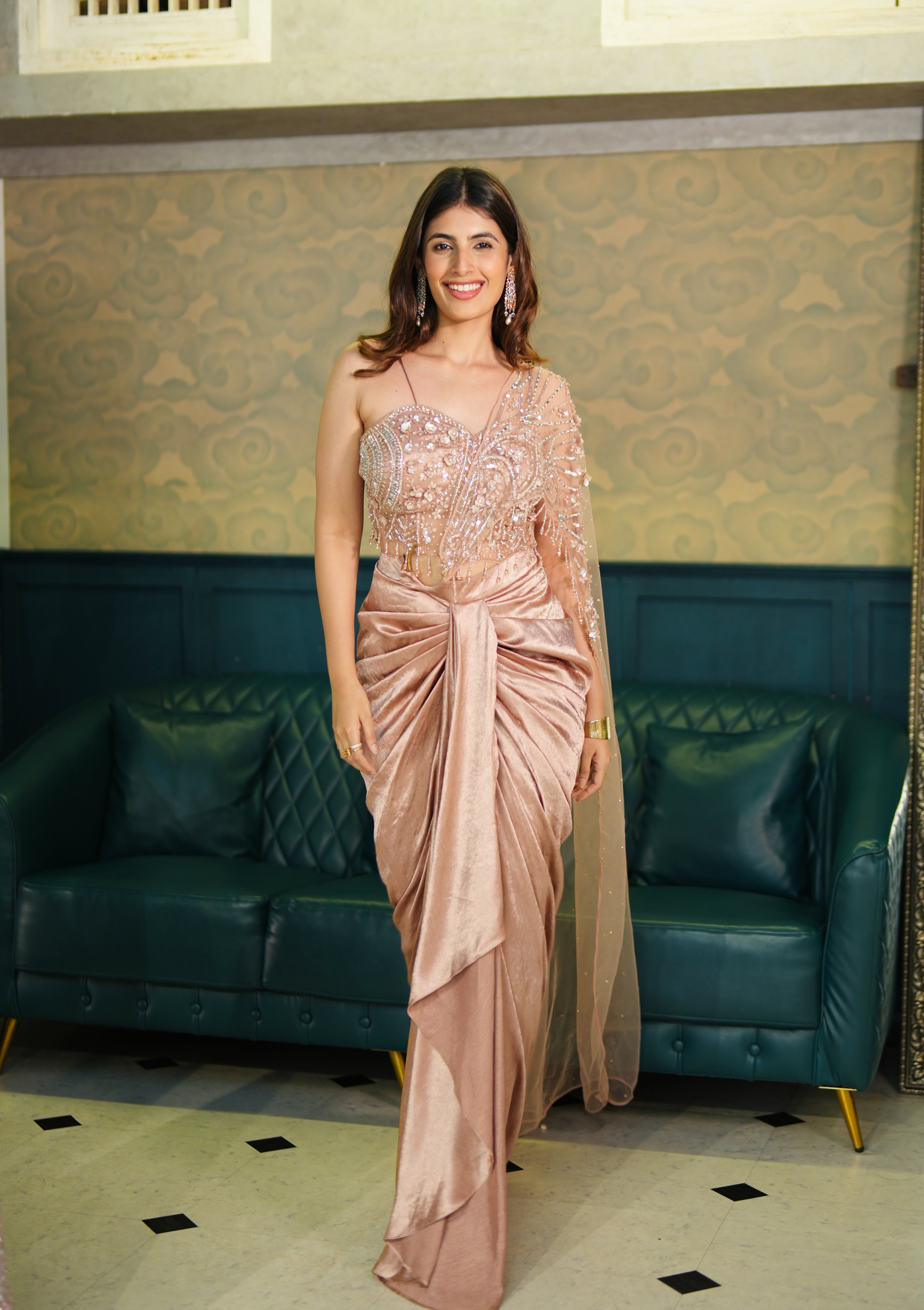 Woman in a pink drake skirt set standing in a room with green sofas and patterned walls.