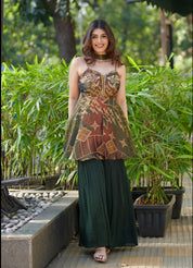 Woman in a patterned top and green pants standing outdoors with greenery in the background