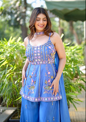 Woman wearing a blue embroidered outfit standing outdoors with greenery in the background